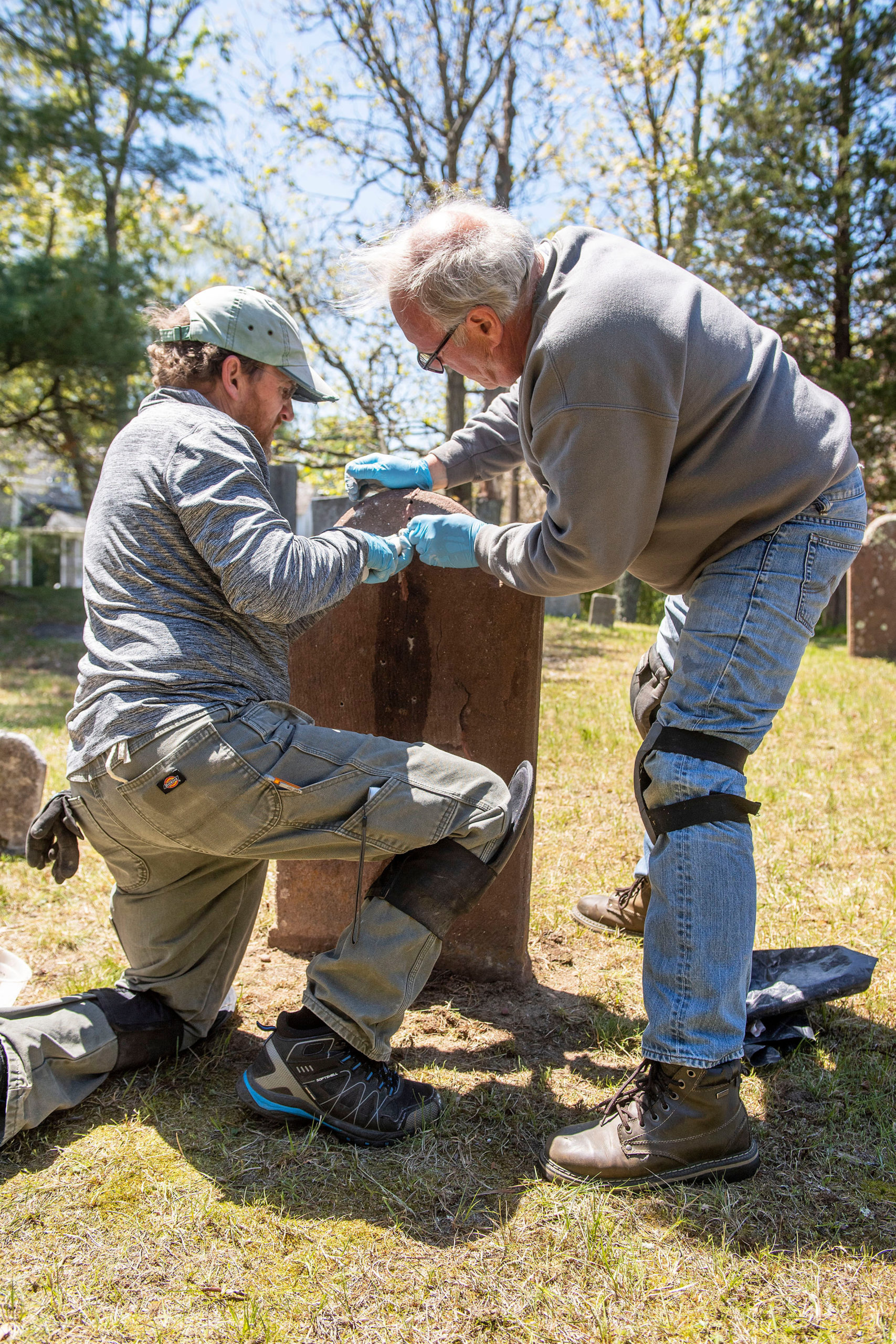 Materials Conservator Joel Snodgrass and Burying Ground Preservation Group Partner Zach Studenroth inject a liquid grout compound into a brownstone headstone during the early stages of the renovation and preservation process taking place at the Old Burying Ground adjacent to the Sag Harbor Old Whalers Church on May 11.     MICHAEL HELLER
