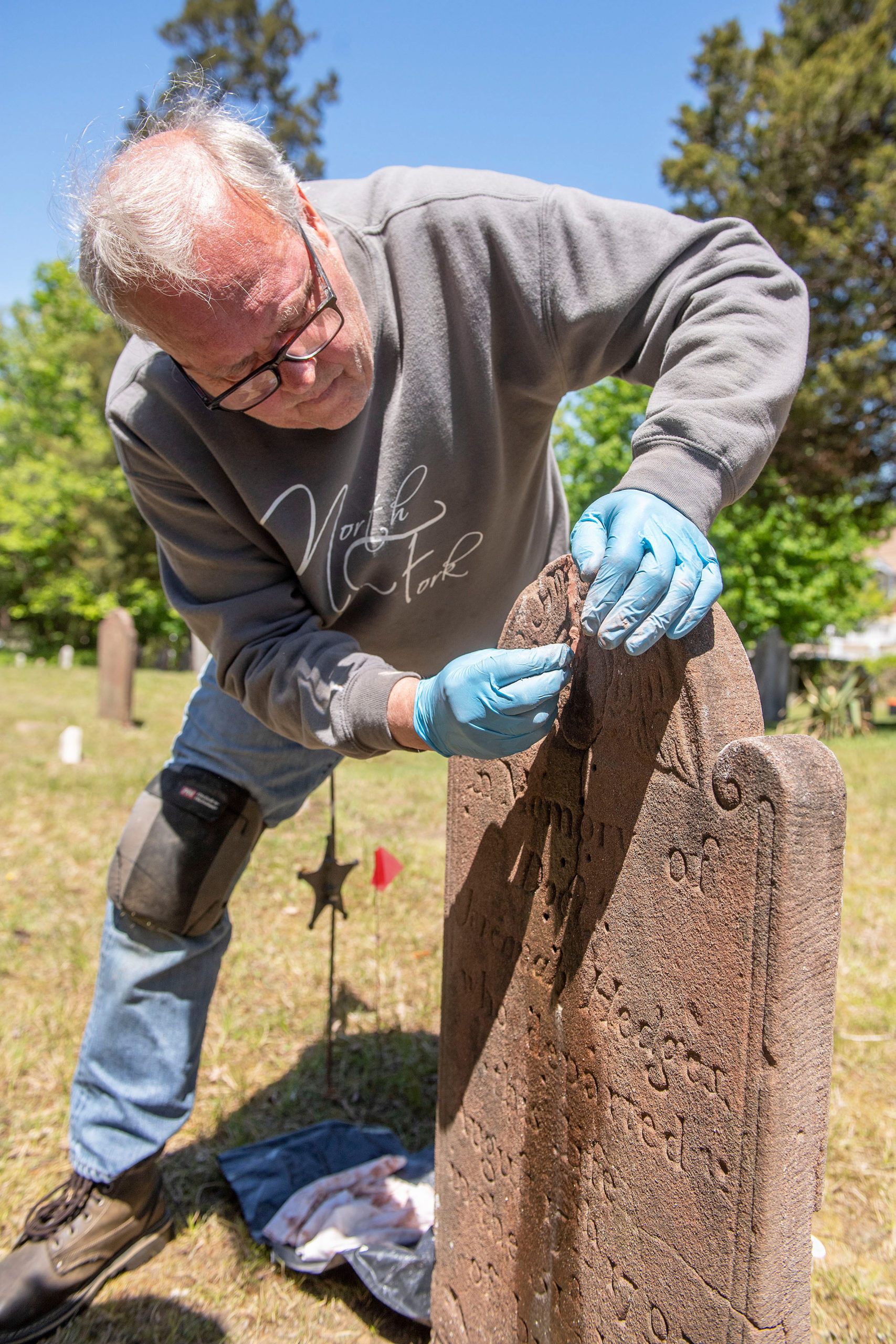 Burying Ground Preservation Group Partner Zach Studenroth applies a grout compound onto a brownstone headstone during the early stages of the renovation and preservation process taking place at the Old Burying Ground adjacent to the Sag Harbor Old Whalers Church on May 11.    MICHAEL HELLER