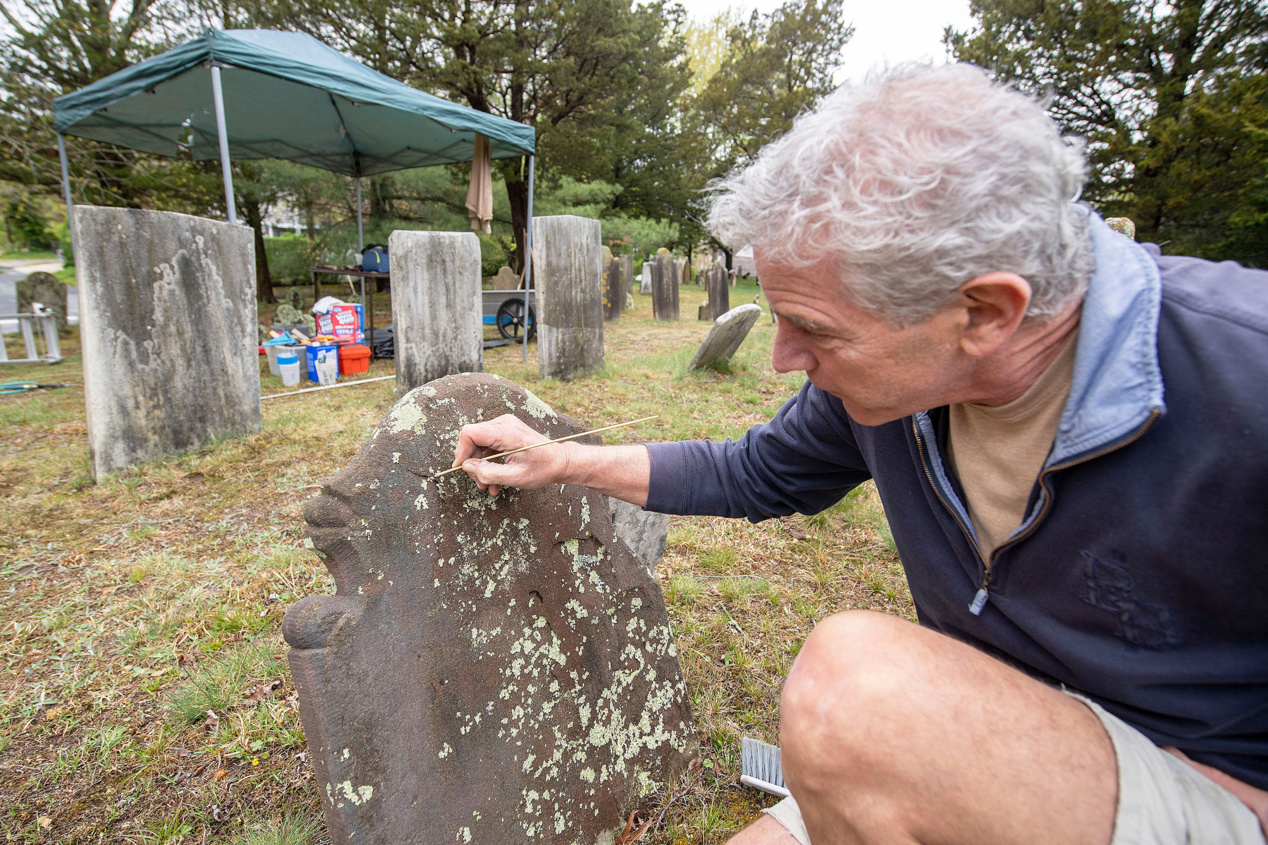 Burying Ground Preservation Group Partner Kurt Kahofer scrapes lichen off of a headstone during the early stages of the renovation and preservation process taking place at the Old Burying Ground adjacent to the Sag Harbor Old Whalers Church on  May 4.  MICHAEL HELLER