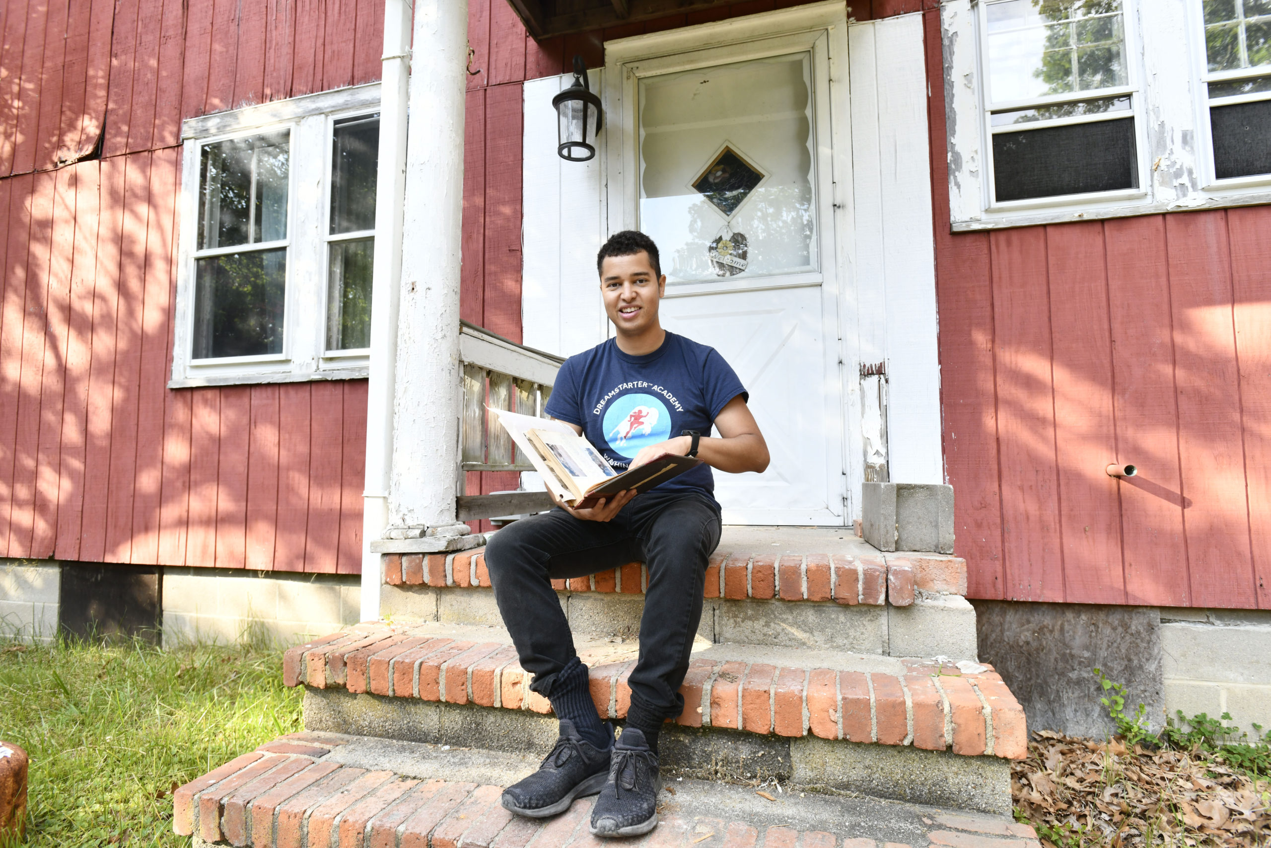 Jeremy Dennis on the steps of Ma's House with a family album during the 2020 renovation of the property.