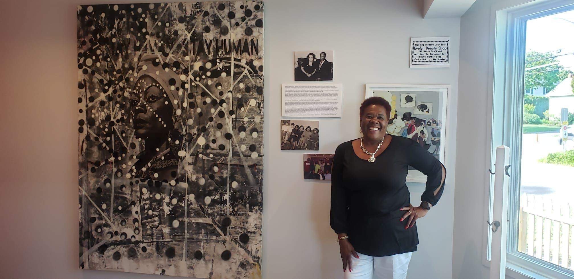 Southampton African American Museum Executive Director Brenda Simmons next to a painting that will be part of the interactive experience being integrated into the museum this spring. The painting will provide a jumping off point for visitors to learn about Black hairstyles and the history and culture surrounding Black hair care for women.