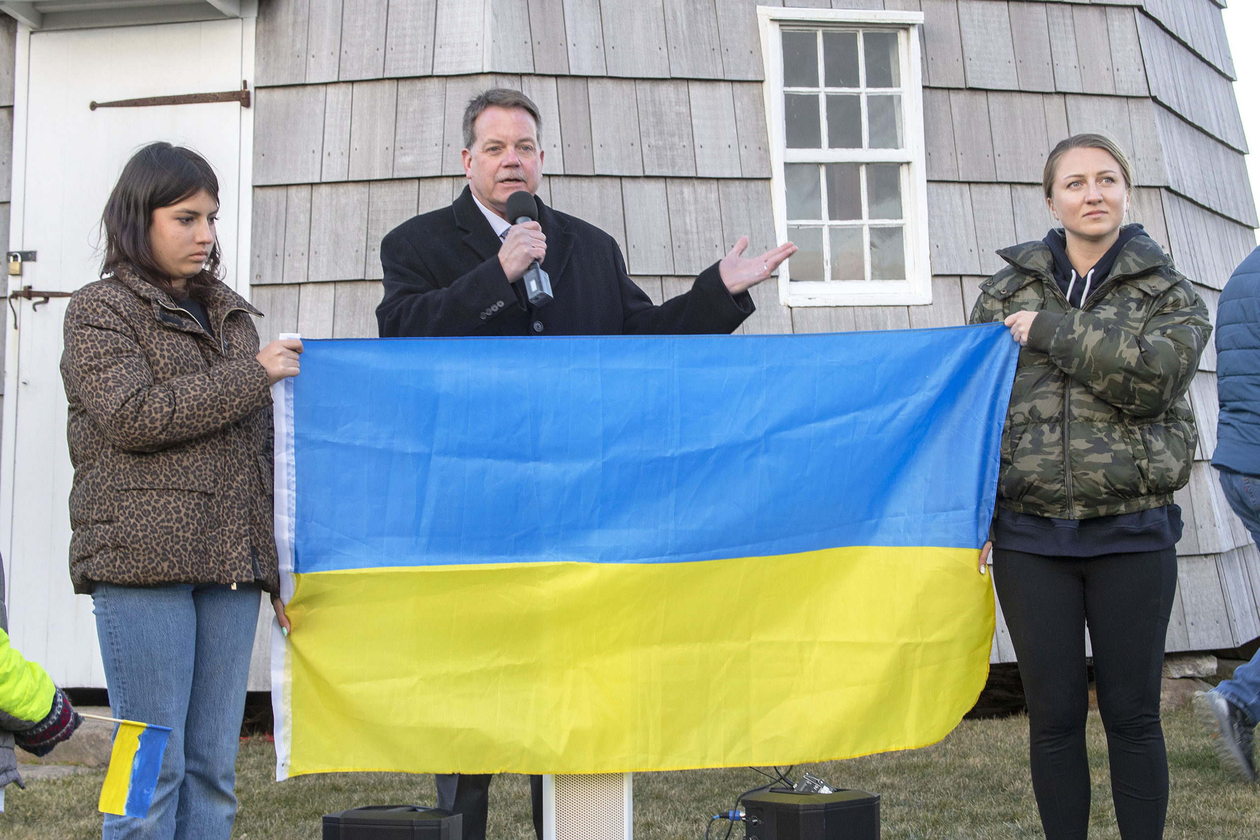 East Hampton Village Mayor Jerry Larsen speaks as Anya Bimson, right, and her daughter, Vira Palamarchuk, whose father is fighting on the front lines in Ukraine, hold up a Ukrainian flag during a rally last Thursday on the Hook Mill Village Green in East Hampton. MICHAEL HELLER