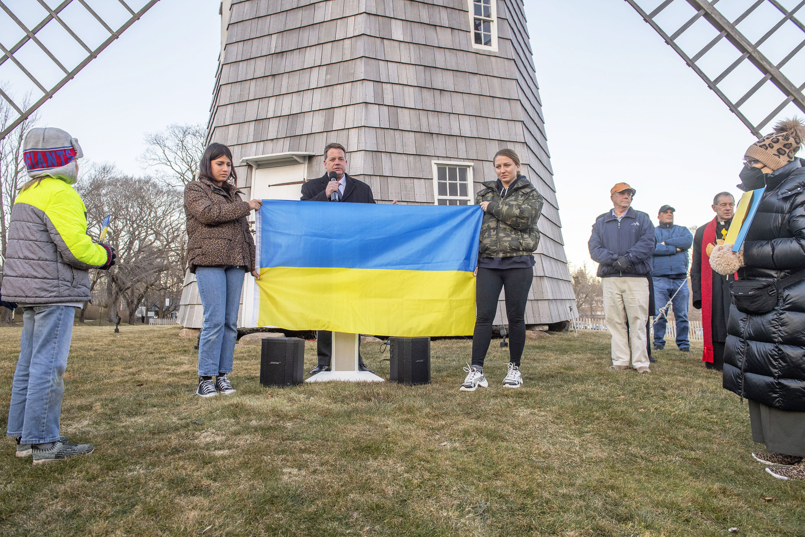 East Hampton Village Mayor Jerry Larsen speaks as Anya Bimson, right, and her daughter, Vira Palamarchuk, whose father is fighting on the front lines in Ukraine, hold up a Ukrainian flag during a rally last Thursday on the Hook Mill Village Green in East Hampton. MICHAEL HELLER