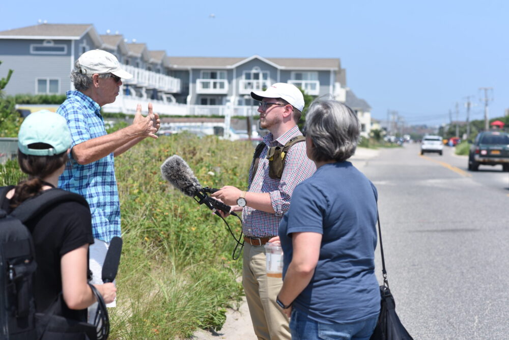 J.D. Allen, right, interviews Kevin McAllister, left, founder of Defend H2O, in Montauk, as producer Sabrina Garone, left foreground, and Alison Branco, coastal director at The Nature Conservancy, listen on.
