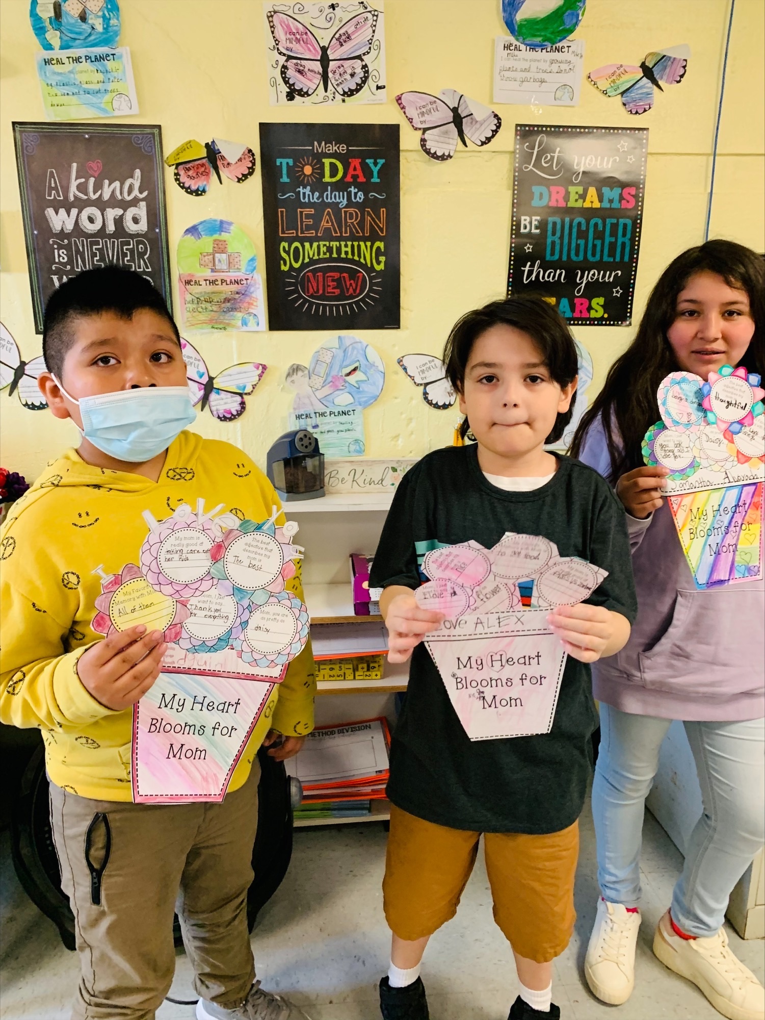Hampton Bays Elementary School fourth grade students in Krista Savino’s class used their writing skills to carefully craft special Mother’s Day gifts. They each decorated a colorful flower and adorned it with writings about their favorite memories of their mom. With their gifts, from left,  left,  Eguin Puin Faraz, Alex Sandoval and Samantha Alvarado. COURTESY HAMPTON BAYS SCHOOL DISTRICT