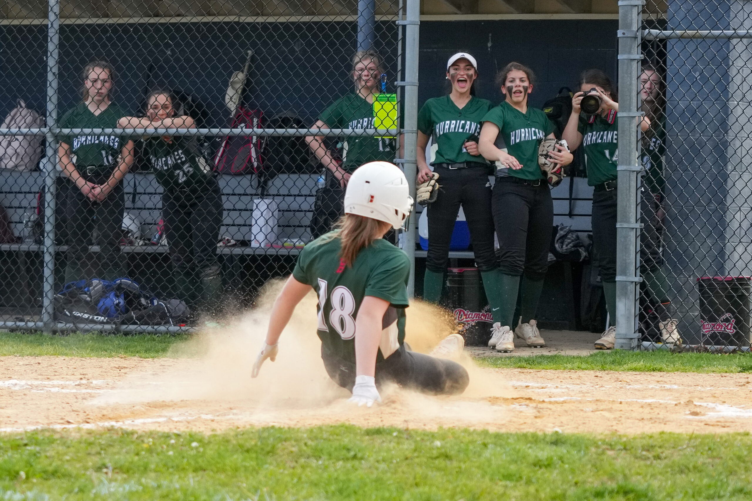 Kali Baumiller slides into home plate with her teammates watching from the dugout.   RON ESPOSITO