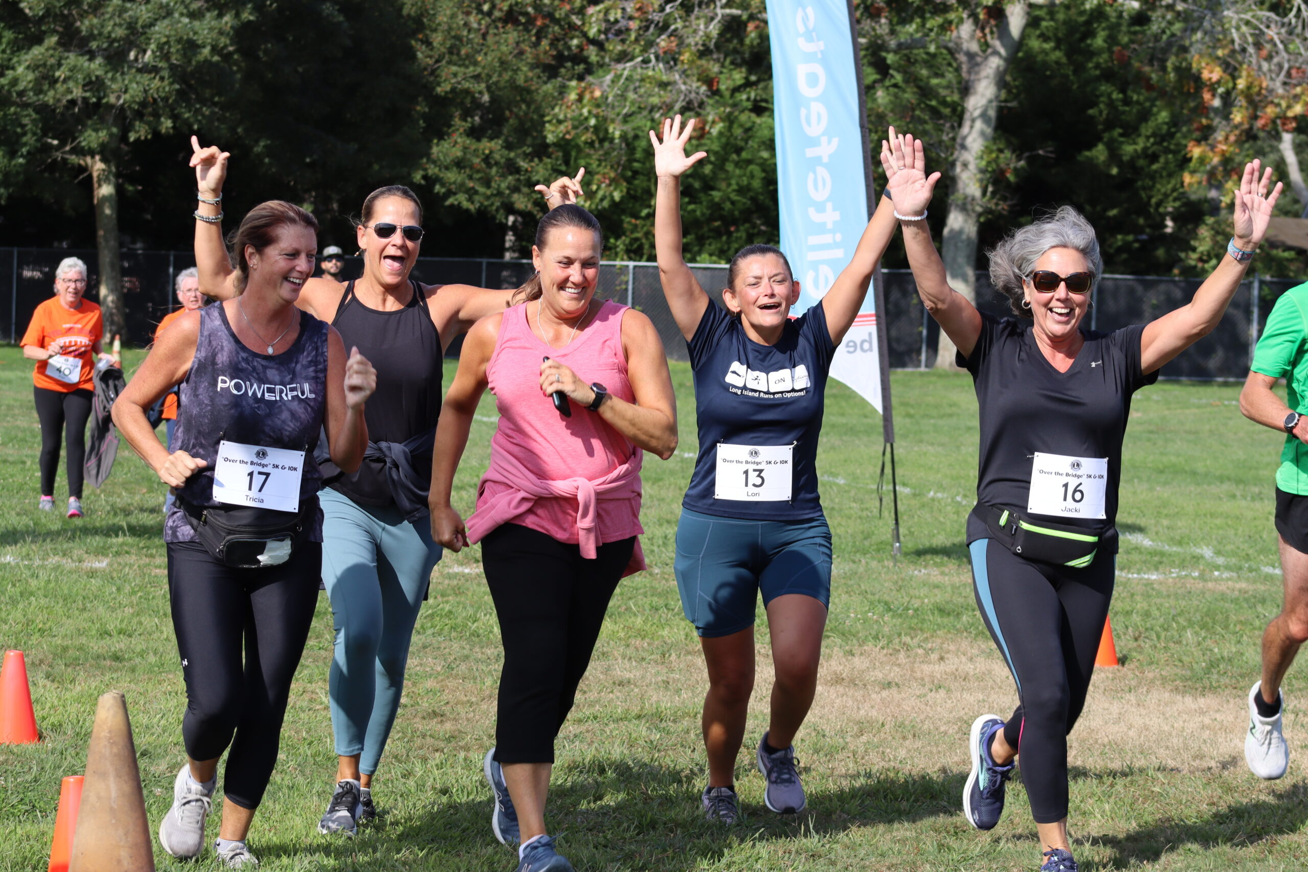A group of friends raises their hands in triumph after crossing the finish line in the 11th annual Over the Bridge 5K and 10K run in Hampton Bays on Saturday. CAILIN RILEY