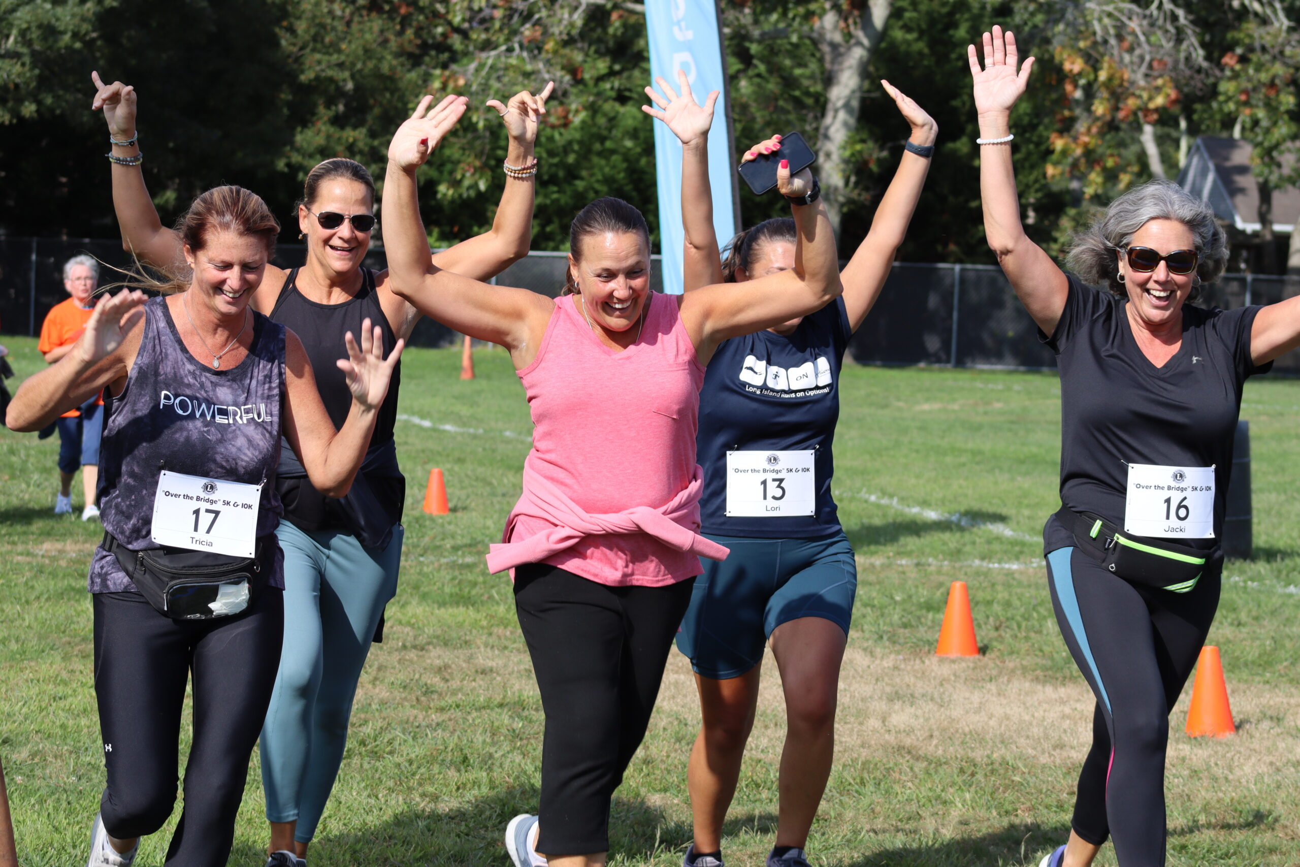A group of friends raises their hands in triumph after crossing the finish line in the 11th annual Over the Bridge 5K and 10K run in Hampton Bays on Saturday. CAILIN RILEY