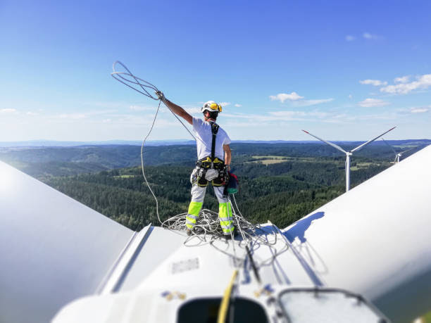 A wind turbine technician harnessed in, on top of a wind turbine.