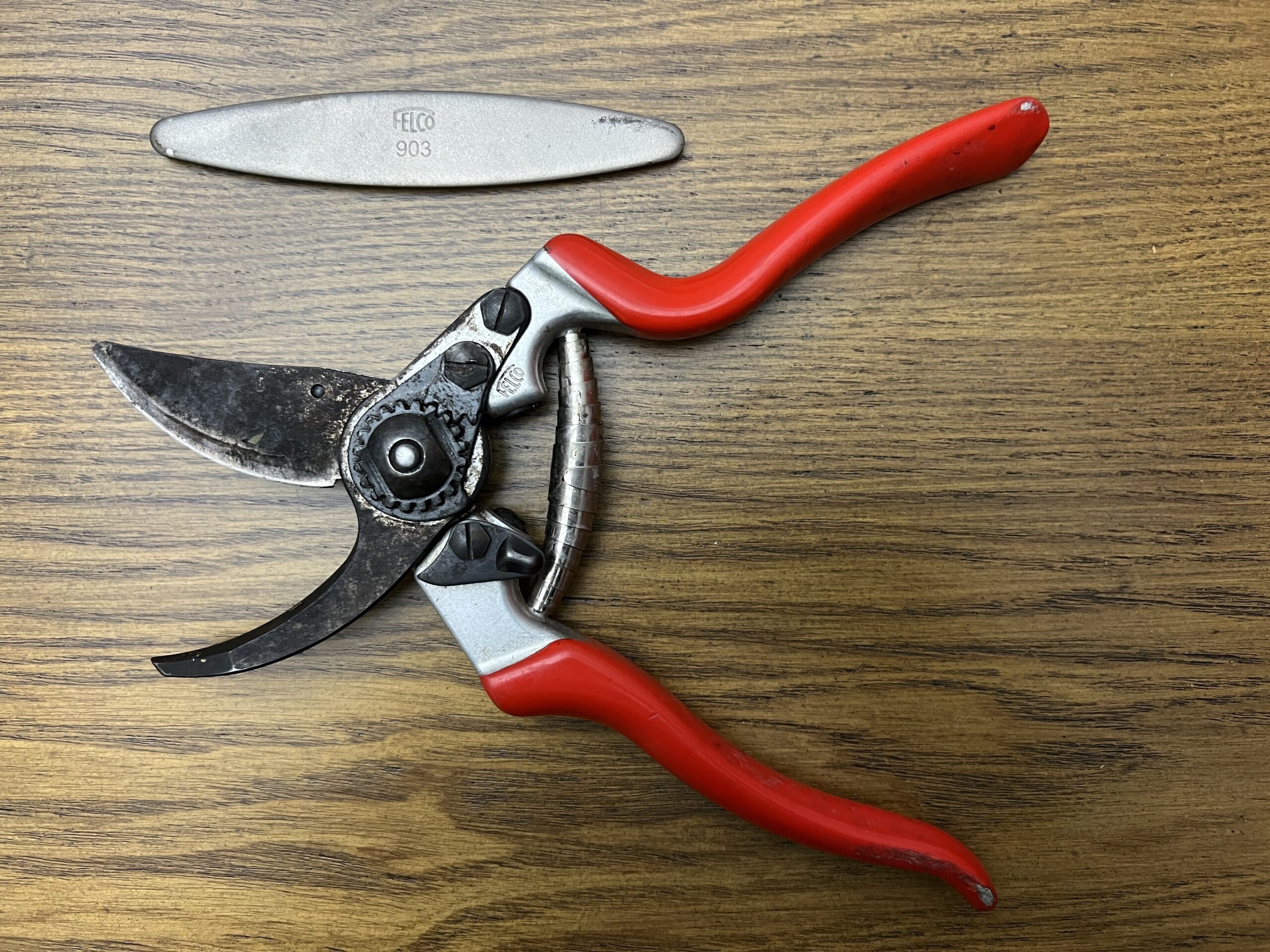 Pruners like this well-used Felco #2 should be sharpened before every use for clean cuts.  Above the pruner is a Felco #903 sharpening tool. Neither is inexpensive but used together the pruner will last for years.
